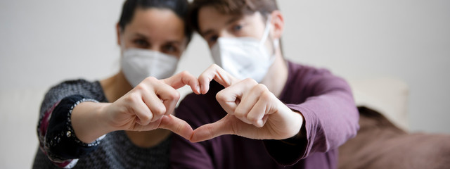 couple with face mask doing a heart with their hands