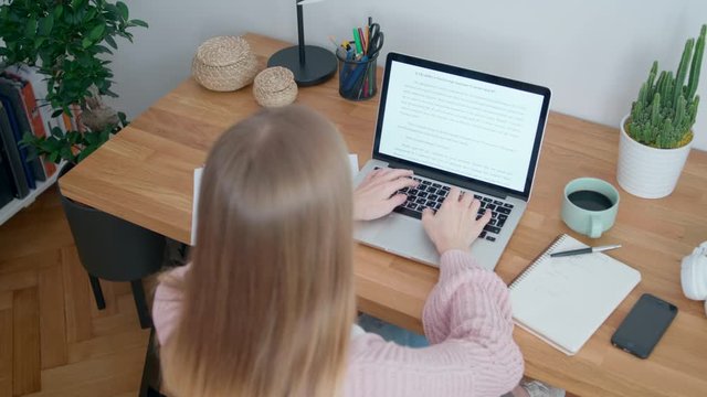 Young Woman Works in Home Office using Laptop. Female Student or Copywriter is Typing in Text Editor Sitting at Wooden Desk. Self-isolation concept at Coronavirus Pandemic. 4K Top View Orbit Shot