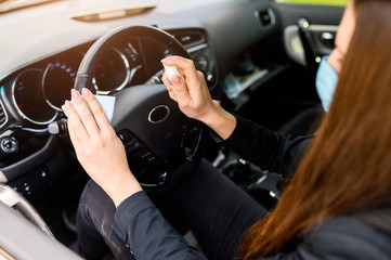 The girl in the car with a medical mask on a face is disinfecting the steering wheel with an antiseptic to protect herself from viruses. Coronavirus pandemia, epidemia covid-19