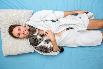 Smiling man with cat lying in bed