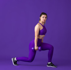 Strong. Beautiful young female athlete practicing in studio, monochrome purple portrait. Sportive fit caucasian model with weights. Body building, healthy lifestyle, beauty and action concept.