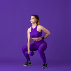 Fototapeta na wymiar Strong. Beautiful young female athlete practicing in studio, monochrome purple portrait. Sportive fit caucasian model with weights. Body building, healthy lifestyle, beauty and action concept.
