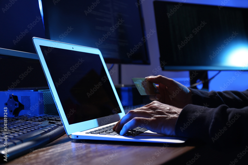 Poster hacker with computers and credit card in dark room, closeup. cyber crime