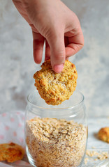 Oatmeal cookies in the hand. Oatmeal in a glass jar. Light wooden background. Healthy sweet breakfast. Free space for text. Close-up. Vertical view.