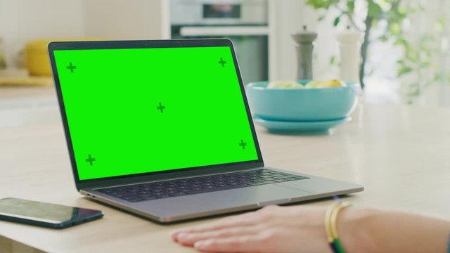 Close Up Green Screen Mock Up on a Laptop Computer. Device is Used on a Kitchen Table in a Modern Home. Person Uses Touch Pad and Presses Enter. Sunny Modern Kitchen with Healthy Lifestyle Vibes.