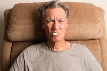 Obraz premium Senior Man at home checking his Temperature on a digital thermometer