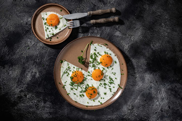 Fried eggs on a ceramic plate with herbs, knife and fork