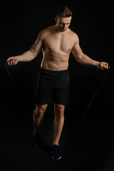 Sporty man with jumping rope on dark background