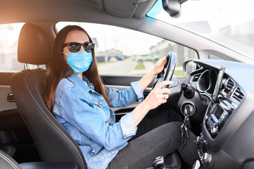 A young woman in a medical mask and in sunglasses is driving a car. Coronavirus pandemia, epidemia...