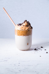 Dalgona coffee in a glass with chocolate chips and bamboo straw on white background. Vertical picture.