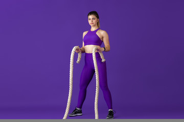 Active. Beautiful young female athlete practicing in studio, monochrome purple portrait. Sportive caucasian fit model with ropes. Body building, healthy lifestyle, beauty and action concept.