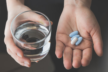 hand holding pills and glass of water