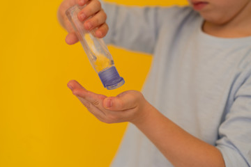 children’s hand holds bottle of transparent hand sanitizer gel on yellow background. Hand hygiene. kids hygiene. Bacteria and virus protection