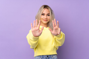 Teenager girl wearing a yellow sweatshirt over isolated purple background counting nine with fingers