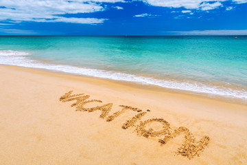 Fototapeta premium Vacation text on a beach. Vacation written in a sandy tropical beach. 
