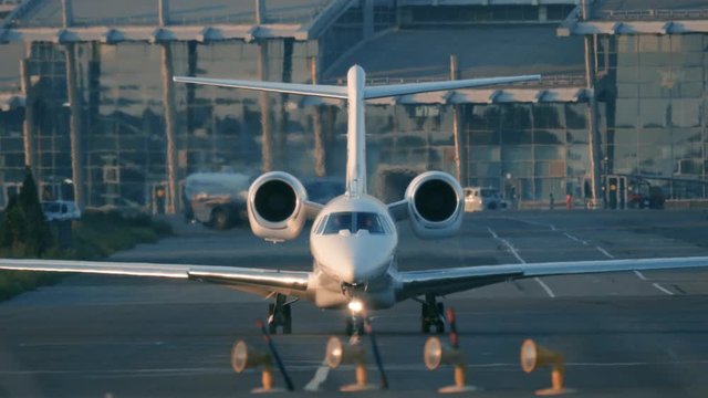 Business jet (private jet) is taxiing on the taxiway before taking off at sunset. Front view