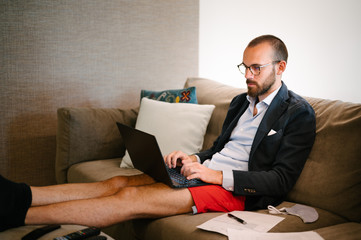 Young man working from home sitting on the sofa with suit and training shorts