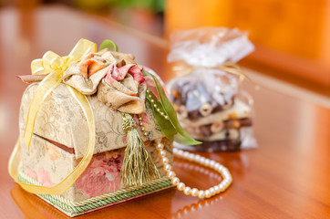 Gift box with yellow and green ribbon bow and pearl jewelry on wooden table with chocolate treats 