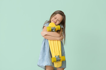 Happy little girl with skateboard on color background