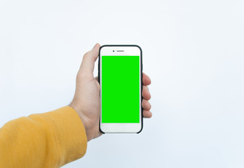 POV, male hand in a yellow sweater holding smartphone with blank green screen chromakey on a white background. Selfie concept. First-person view