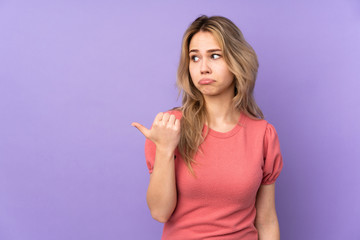 Teenager Russian girl isolated on purple background unhappy and pointing to the side