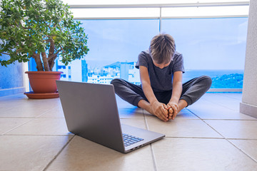 Boy with laptop computer doing sport exercises, practicing yoga on balcony. Sport, healhty...