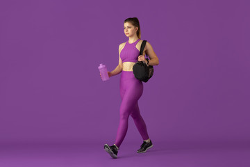 Fototapeta na wymiar Beautiful young female athlete practicing in studio, monochrome purple portrait. Sportive caucasian fit model going to training with bag. Body building, healthy lifestyle, beauty and action concept.