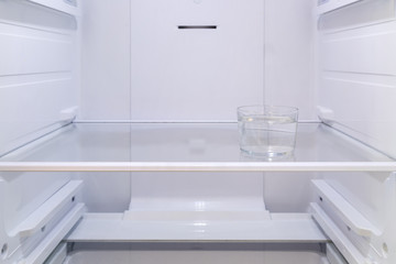 a glass of water on the shelf in the empty refrigerator