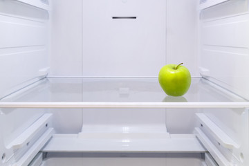 one green Apple on a shelf in an empty refrigerator