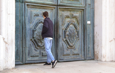 Fototapeta na wymiar A young tourist looks at the beautiful old door of the temple in Venice.