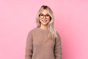 Teenager blonde girl wearing a sweater over isolated pink background with glasses and happy