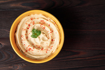 Plate of spicy traditional hummus with pepper and greens on a wooden background. Top view.