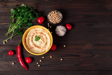 Plate of spicy traditional hummus with pepper and greens on a wooden background. Colorful hummus bowls decorated with chickpeas, herbs, garlic, tomate and chili pepper. Top view