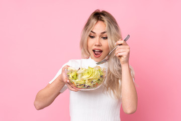 Teenager blonde girl holding a salad over isolated pink wall