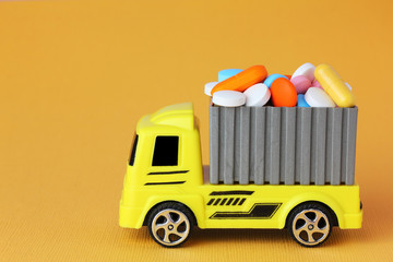 pharmaceuticals supply concept. A yellow toy truck delivering pills and drugs in a container