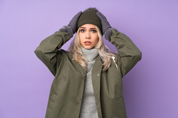 Teenager blonde girl with winter hat over isolated purple background frustrated and takes hands on head