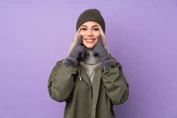 Teenager blonde girl with winter hat over isolated purple background smiling with a happy and pleasant expression