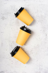 Yellow paper cups, light grey concrete background. Flatlay. Coffee to go concept. Place for text on the right and left. Copy space. Minimalism. Mock up.
