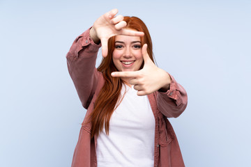 Redhead teenager girl over isolated blue background focusing face. Framing symbol