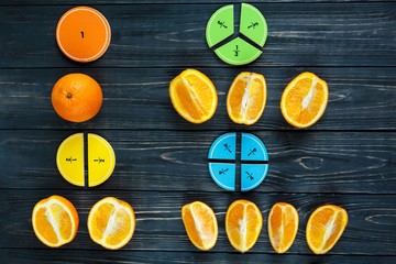 Сolorful math fractions and oranges as a sample on dark wooden background or table. Interesting...