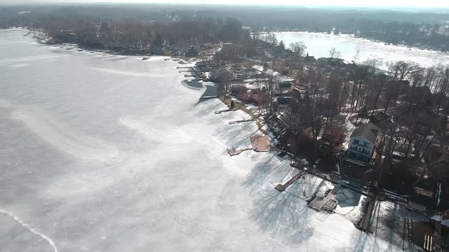 Flying over snow covered houses along frozen icy lakefront, Michigan USA