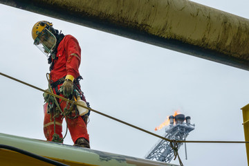 Working at height. An abseiler wearing Personal Protective Equipment (PPE) standing on pipeline with background flare tip burning in the sky.