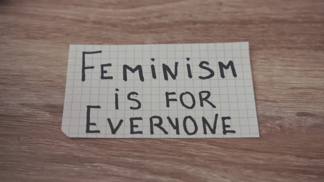 Close up paper on table text Feminism is for Everyone power inside desk woman females feminist girls slow motion