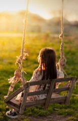 A girl with long hair is sitting on a swing. The concept of childhood, happiness