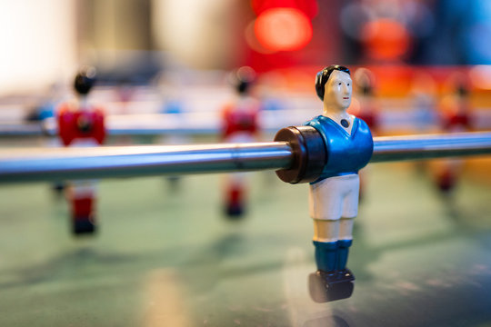 close up on a blue foosball player smiling and looking on the right of  the picture, with a blurred and colorful background.