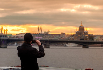 Fototapeta na wymiar A person takes pictures of the city landscape with the sunset and architecture on his phone