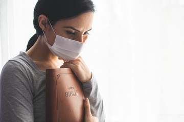 Portrait of a woman with a surgical mask on her face and a bible held tight to her chest