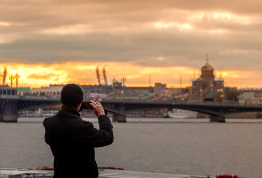 A person takes pictures of the city landscape with the sunset and architecture on his phone