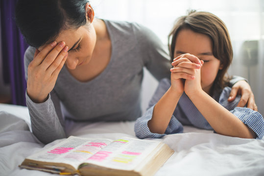 Mother and her daughter reading from bible and praying in their knees near the bed
