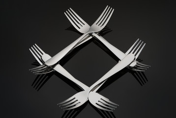 Pattern in the form of a diamond with many silver forks on a black mirror background. Concept,